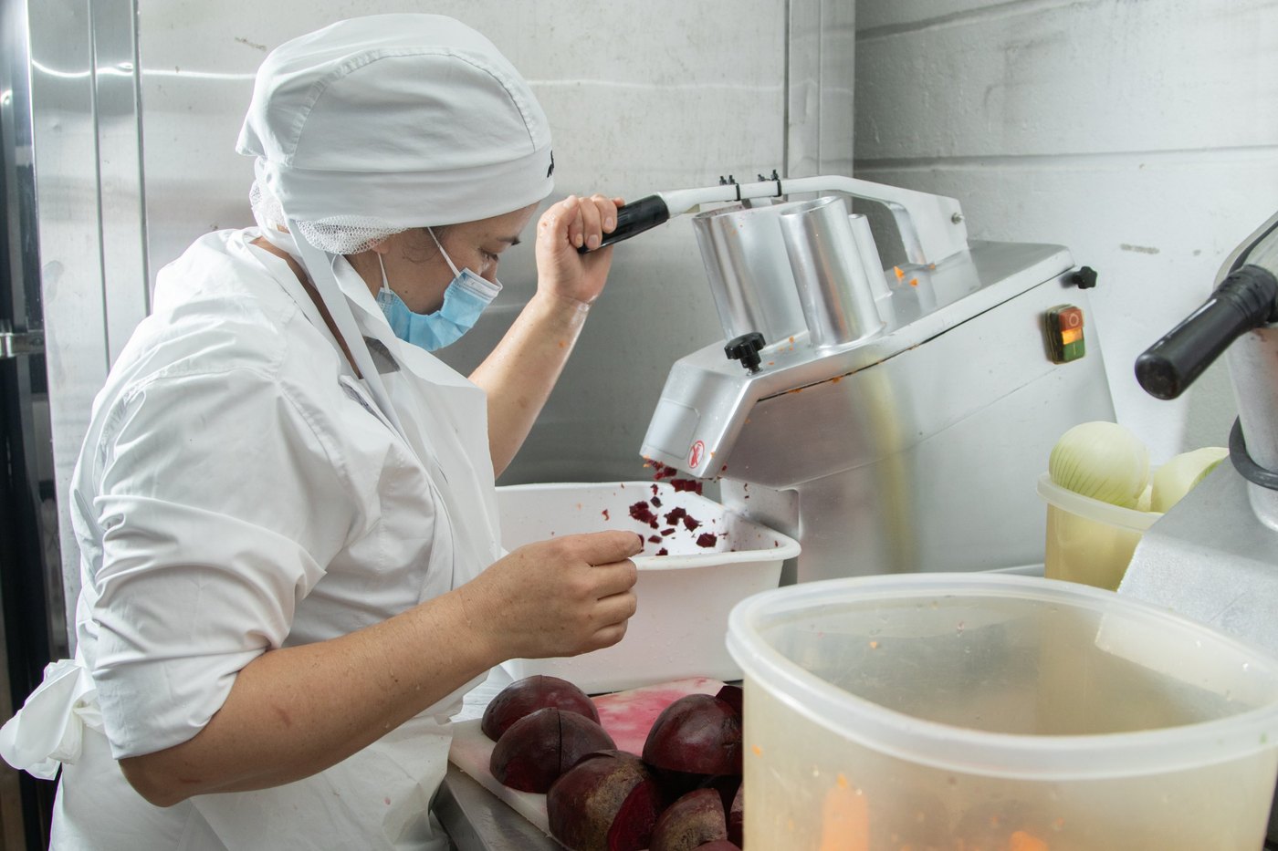 Cocinera de Alabama con gorro, malla y tapabocas procesando remolacha en la planta de producción