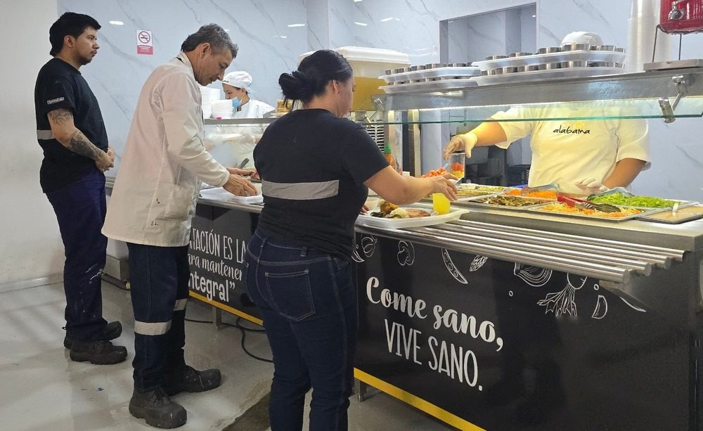 Comedor corporativo operado por Alabama: operarios sirviéndose en la barra de almuerzo atendida por una cocinera de Alabama
